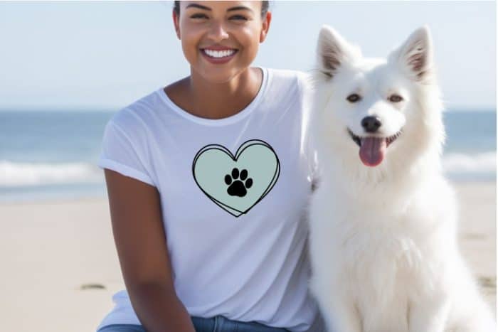 Woman in white shirt sitting with her dog and her shirt has a heart and paw print SVG design in horizontal format