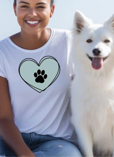 Woman in white shirt sitting with her dog and her shirt has a heart and paw print SVG design in square format