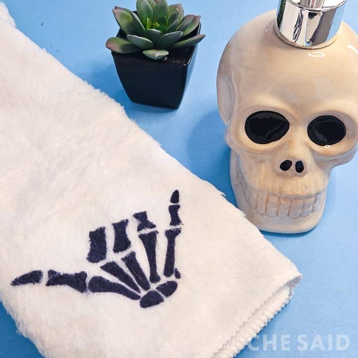 Blue background with skull bathroom soap holder and one white towel with skeleton hand design