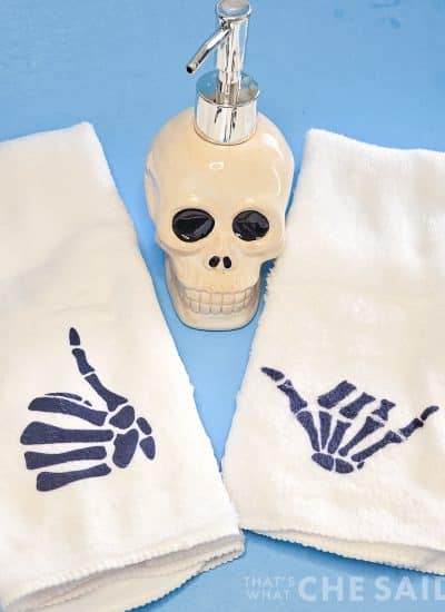 Blue background with skull bathroom soap holder and two white towels with skeleton hands design