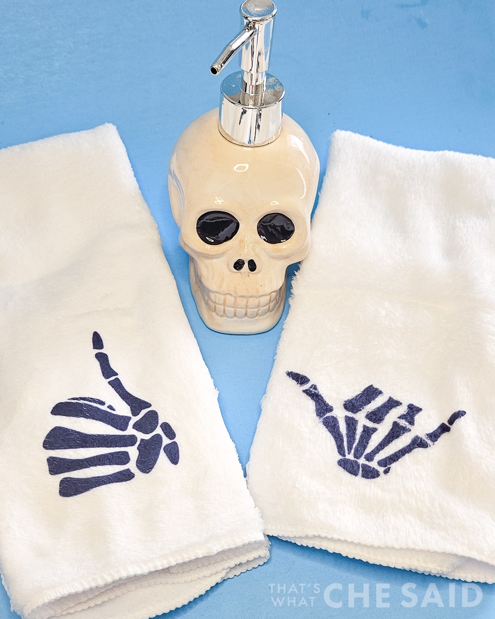 Blue background with skull bathroom soap holder and two white towels with skeleton hands design
