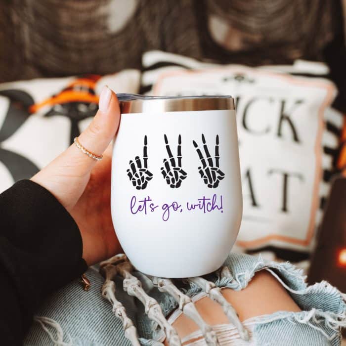 White wine tumbler being held by woman's hand with Halloween decor in background. 123 Let's Go, Wtich! as the design on square format