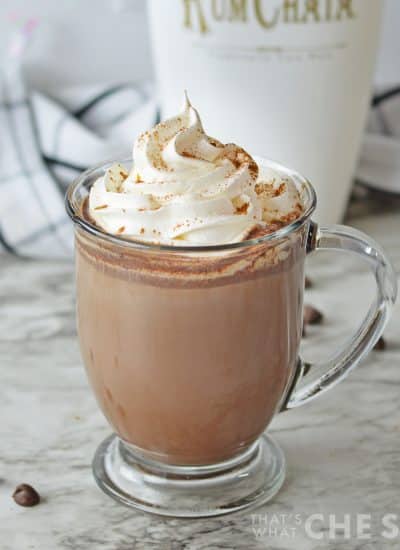Glass mug with rumchata hot cocoa and whipped topping with rumchata bottle in background