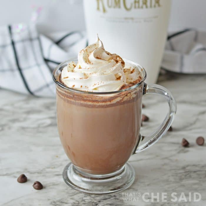 Glass mug with rumchata hot cocoa and whipped topping with rumchata bottle in background