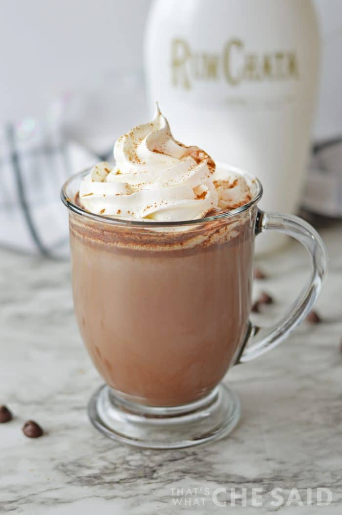 Glass mug with rumchata hot chocolate and whipped topping with rumchata bottle in background