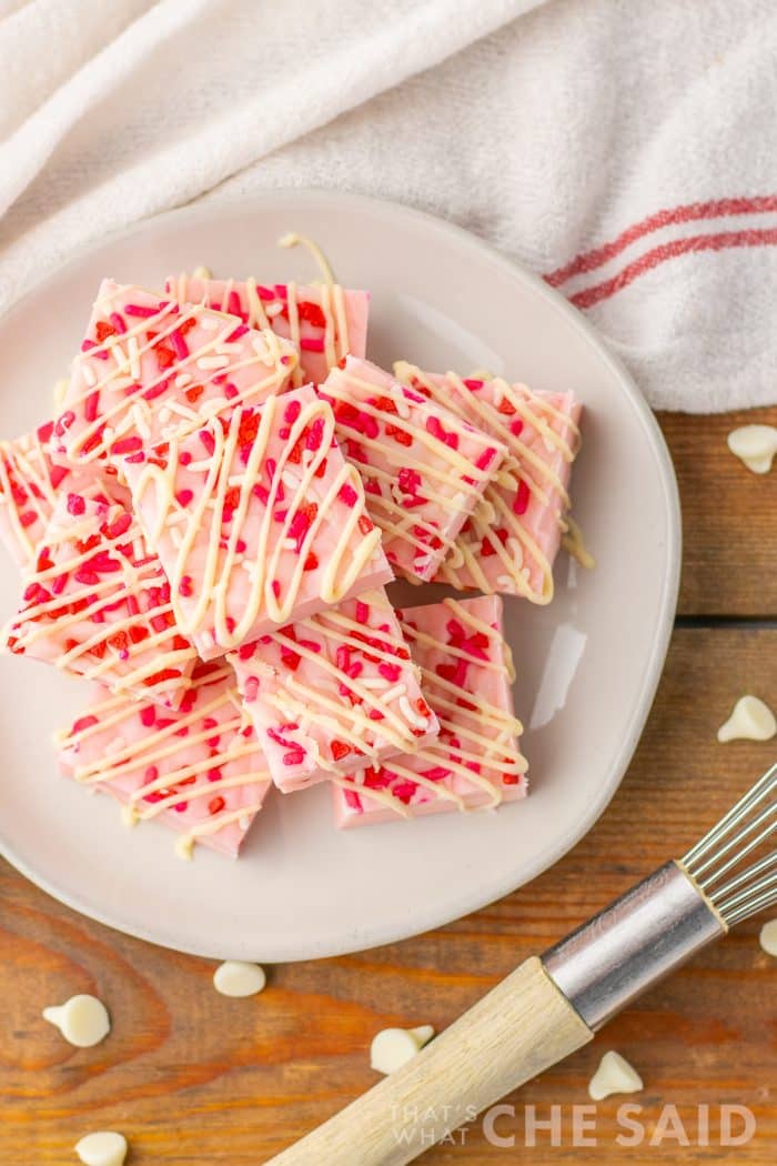 Valentine Sugar Cookie Fudge stacked on a white plate with towel and white chocolate chips Vertical