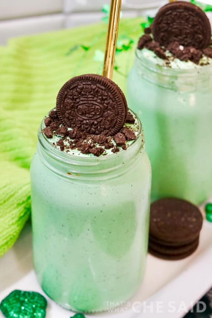Vertical image of a oreo mint milkshakes in mason jars with green towel and gold straw