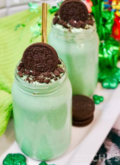 Square image of two oreo mint milkshakes in mason jars with green towel and shamrock decor