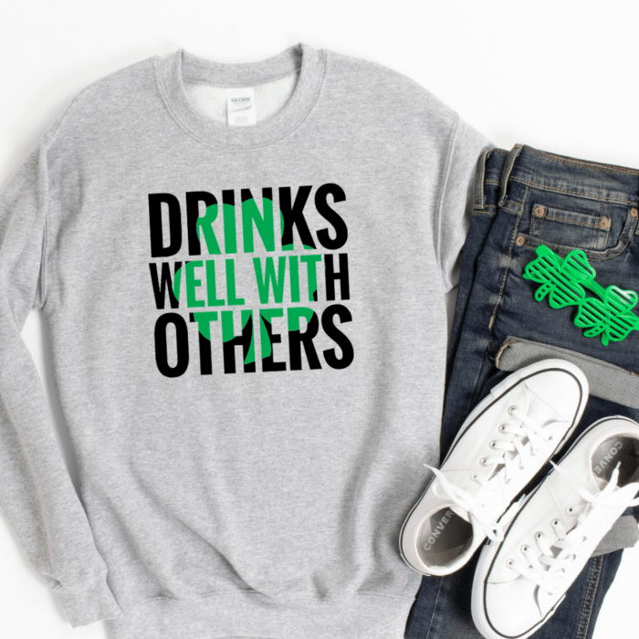 Grey sweatshirt with "Drinks well with others" shamrock design paired with jeans and white converse and shamrock shaped glasses