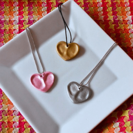 Heart thumbprint pendants on necklaces on white plate with pink backgrond square format