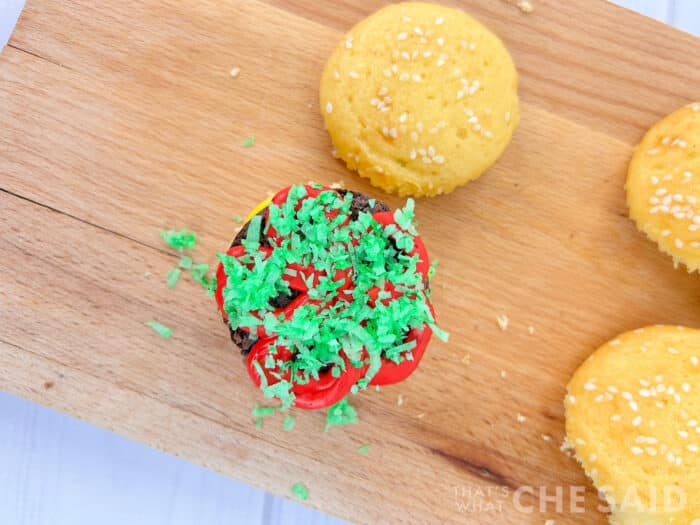 Adding green colored coconut flakes as lettuce for burger cupcakes