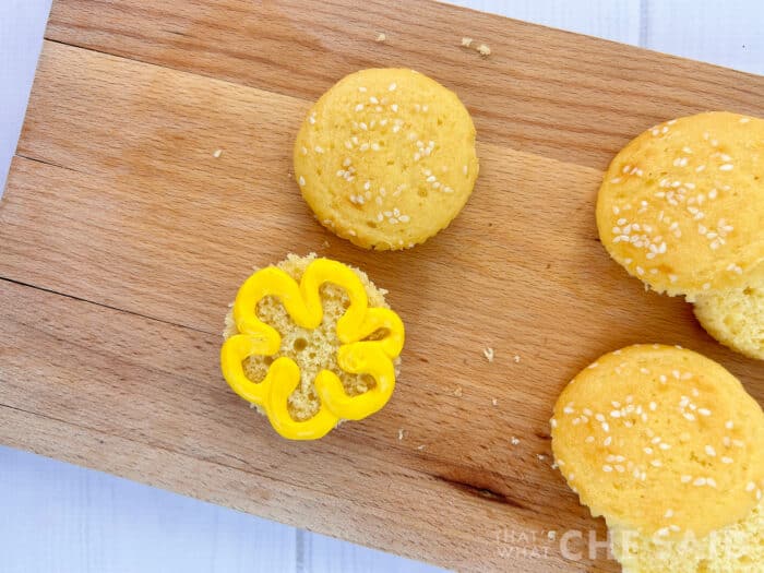 Adding mustard iciing to cupcake burger