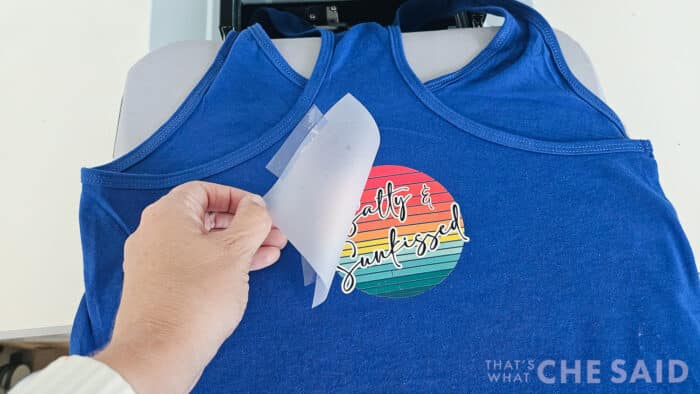 Peeling back the carrier sheet of a pressed DTF design on a blue tank top
