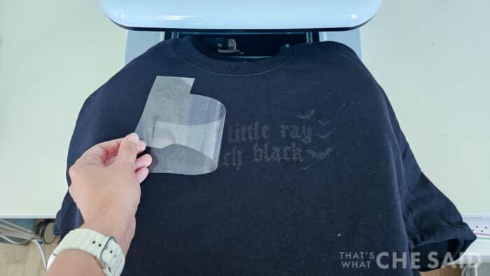 Peeling back the carrier sheet of a pressed glitter iron on design on a black sweatshirt