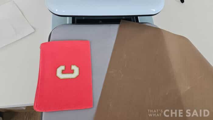 Using the HTVRont Auto Heat Press 2 to press a zippered canvas back with a chenille patch using a teflon protectant sheet