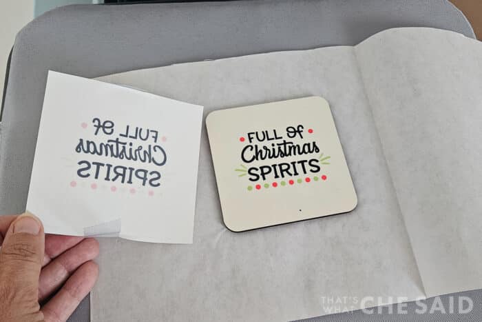 Peeling back the carrier sheet of a pressed sublimation design design on a white coaster