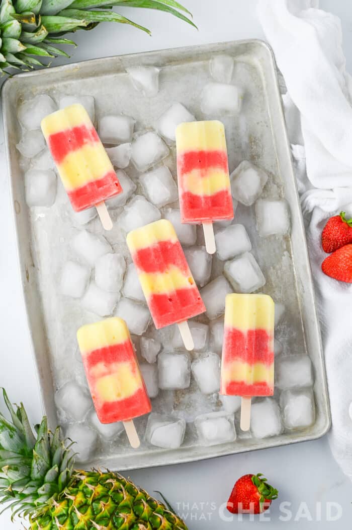 Lava flow popsicles on a baking sheet of ice with pineapples and strawberries on the outskirts