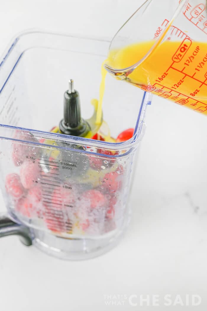 adding juice to blender containing frozen strawberries