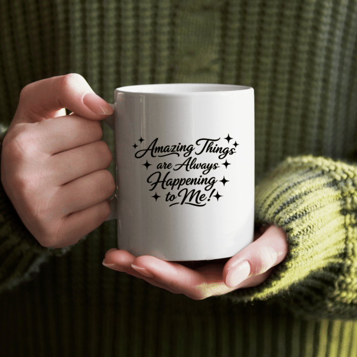 Woman in green sweater holding a white coffee mug with Amazing Things are Always Happening to Me in black